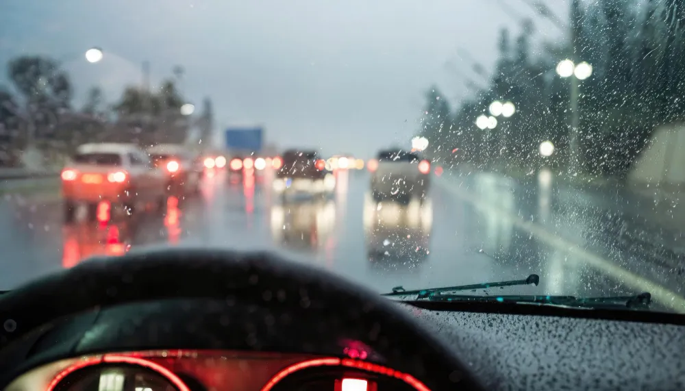 Blick durch eine nasse Windschutzscheibe bei Regen auf dichten Abendverkehr mit roten Rücklichtern