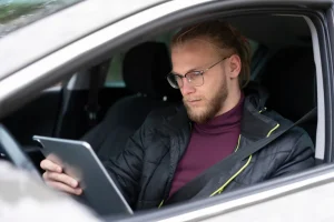 Ein Mann sitzt im Auto und hält ein Tablet in der Hand