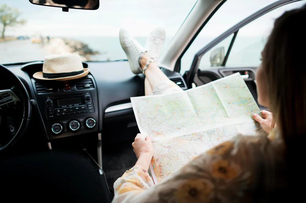 Reisende mit Straßenkarte auf dem Beifahrersitz eines Autos im Urlaub