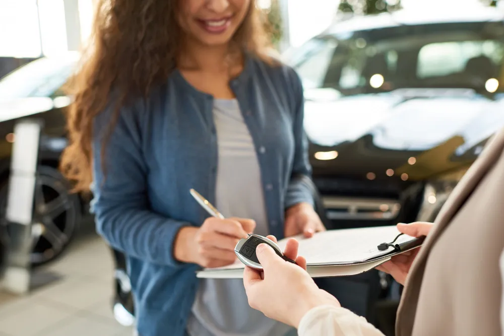 Frau unterschreibt Unterlagen bei einer Fahrzeugübergabe im Autohaus, während ihr ein Autoschlüssel überreicht wird