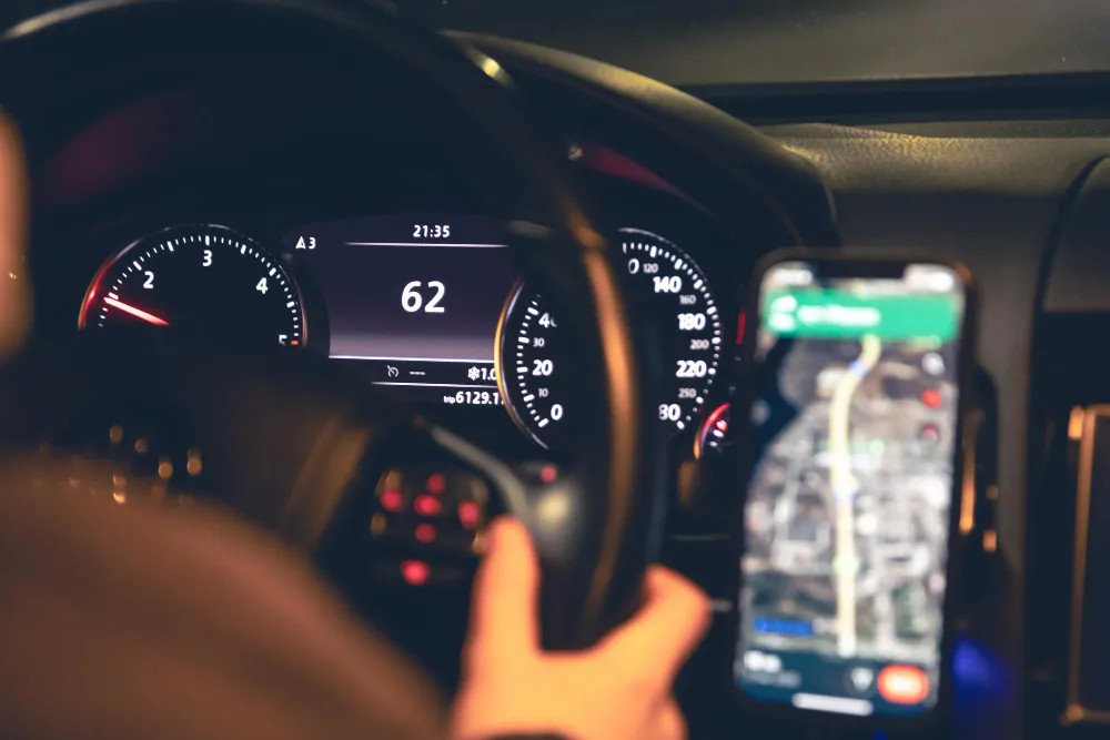 Blick auf Tacho und Smartphone-Navigation während einer Autofahrt im Dunkeln