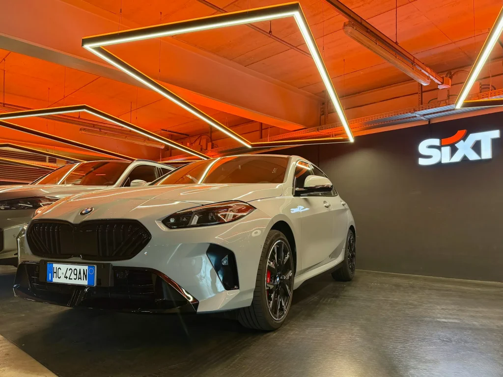 Weißer BMW in einer Sixt-Fahrzeughalle mit orangefarbener Beleuchtung und Sixt-Logo